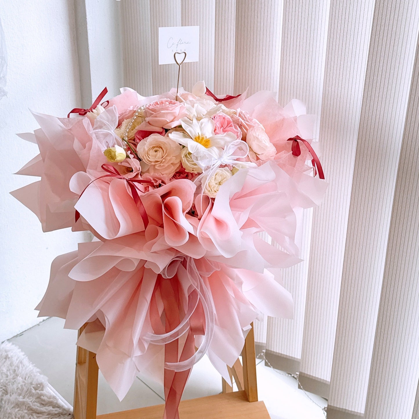 A large, luxurious bouquet of pink flowers including roses, eustomas, ranunculus, tulips, and carnations, arranged in a decorative holder.