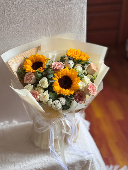 Bouquet of sunflowers and roses wrapped in paper with a white ribbon.