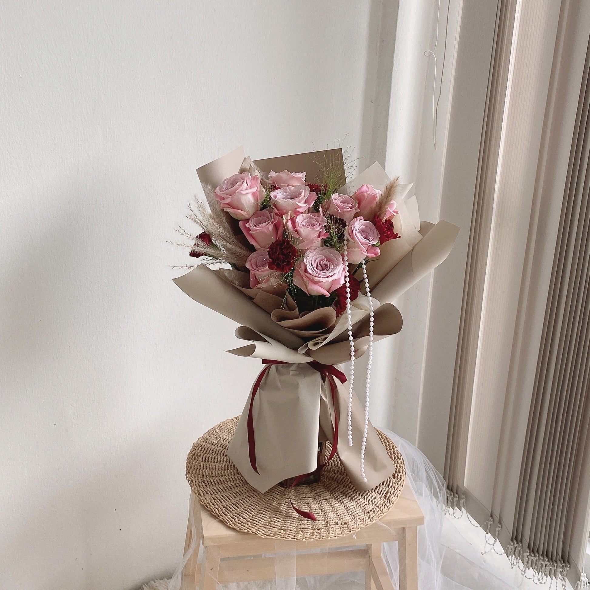 A bouquet of gooseberry pink roses wrapped in beige paper, displayed on a wooden platform with a note attached.