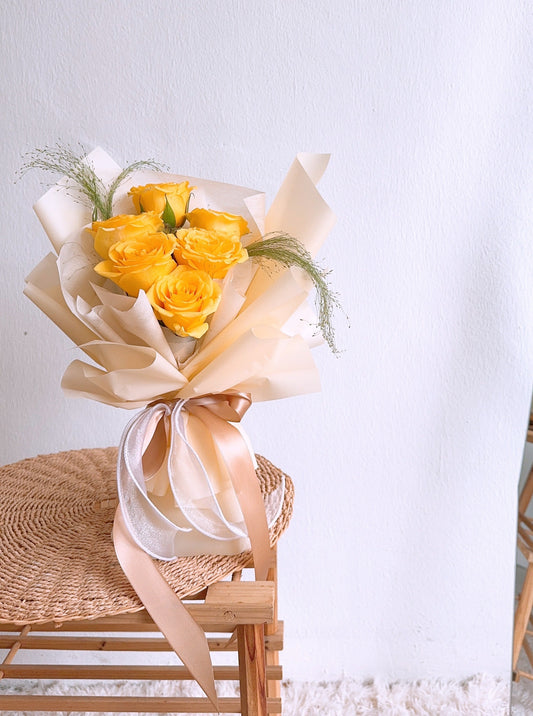 A bouquet of premium yellow roses with light yellow wrapping, displayed on a chair against a light background.
